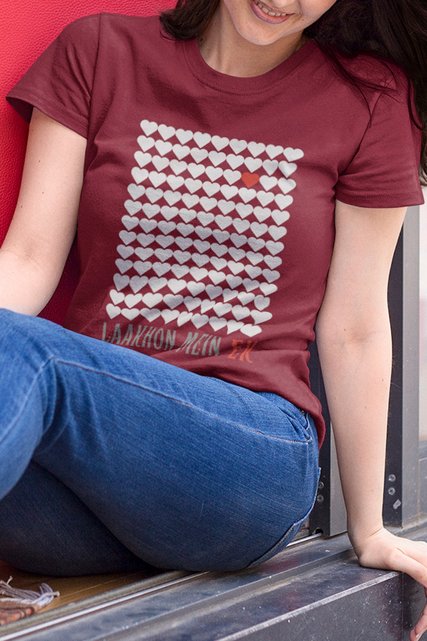 Person wearing a maroon t-shirt with a white graphic design, sitting on a red surface.