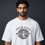 A man wearing a white crew-neck t-shirt with a black graphic print that reads 'JUGAAD EXPERT' around a circular maze design, set against a dark gray studio background.