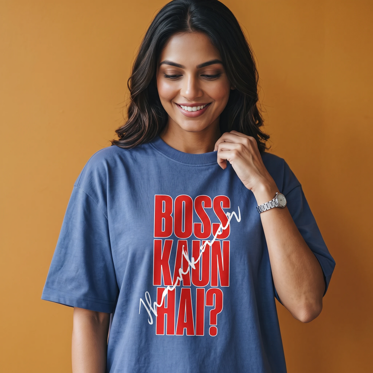 A woman wearing a blue graphic t-shirt with the text 'BOSS KAUN HAI?' in red and white, posing against a solid orange background.