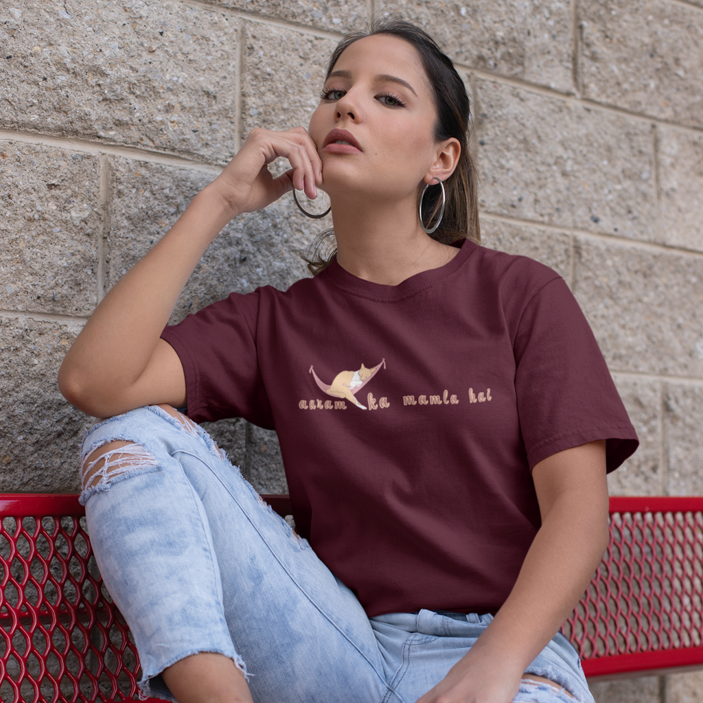Woman wearing a maroon t-shirt with text and graphics, sitting on a red bench against a stone wall.