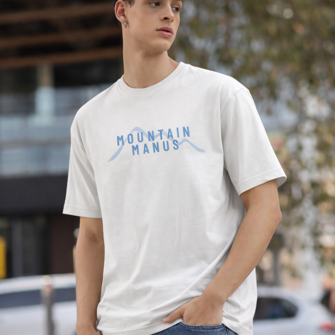 Person wearing a white t-shirt with 'Mountain Manus' text, standing outdoors.