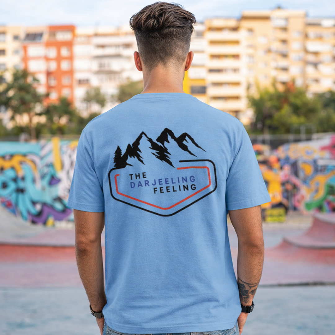 Person wearing a blue t-shirt with 'The Darjeeling Feeling' design in an urban setting.