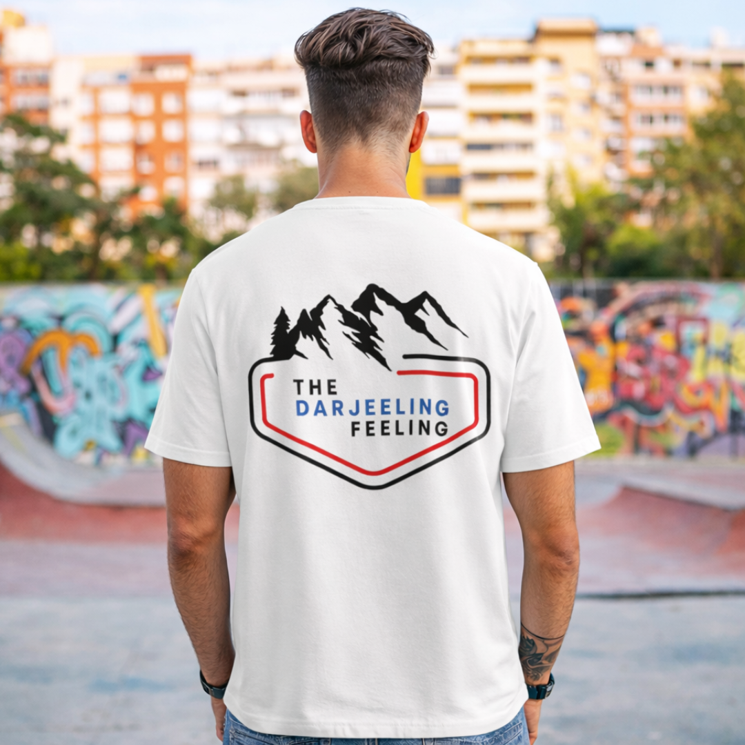 Person wearing a white t-shirt with 'The Darjeeling Feeling' logo in an urban setting.