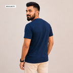 A man wearing a navy blue short-sleeve t-shirt and beige pants, shown from the back and side against a plain beige background. A small label in the top-left corner reads 'REGULAR FIT'.