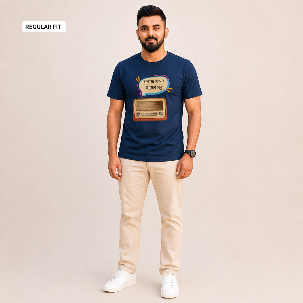 A man modeling a navy blue graphic t-shirt with a retro radio and Bengali text design, paired with beige trousers and white sneakers, against a solid light beige background. A 'REGULAR FIT' label is visible in the top-left corner.