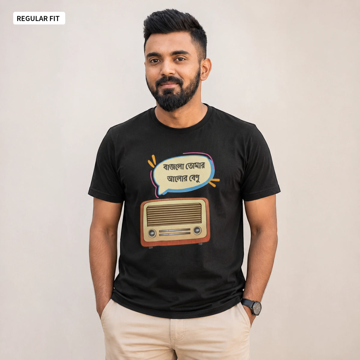 A man wearing a black graphic t-shirt with a retro radio and Bengali text design, paired with beige trousers, standing against a plain beige background.