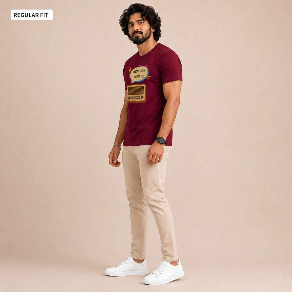 A man modeling a maroon short-sleeve graphic T-shirt with beige pants and white sneakers, standing against a solid beige studio background. A small label in the top-left corner reads 'REGULAR FIT'.