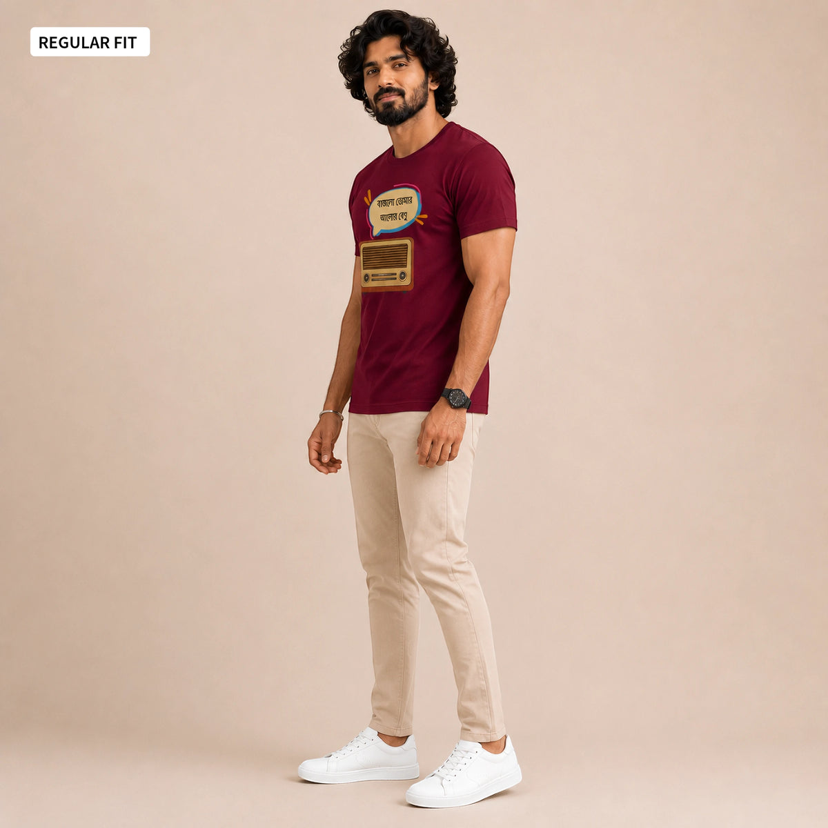 A man modeling a maroon short-sleeve graphic T-shirt with beige pants and white sneakers, standing against a solid beige studio background. A small label in the top-left corner reads 'REGULAR FIT'.