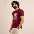 A man wearing a maroon short-sleeve t-shirt with a graphic print of a retro radio and Bengali text, paired with beige pants, standing against a plain beige background.
