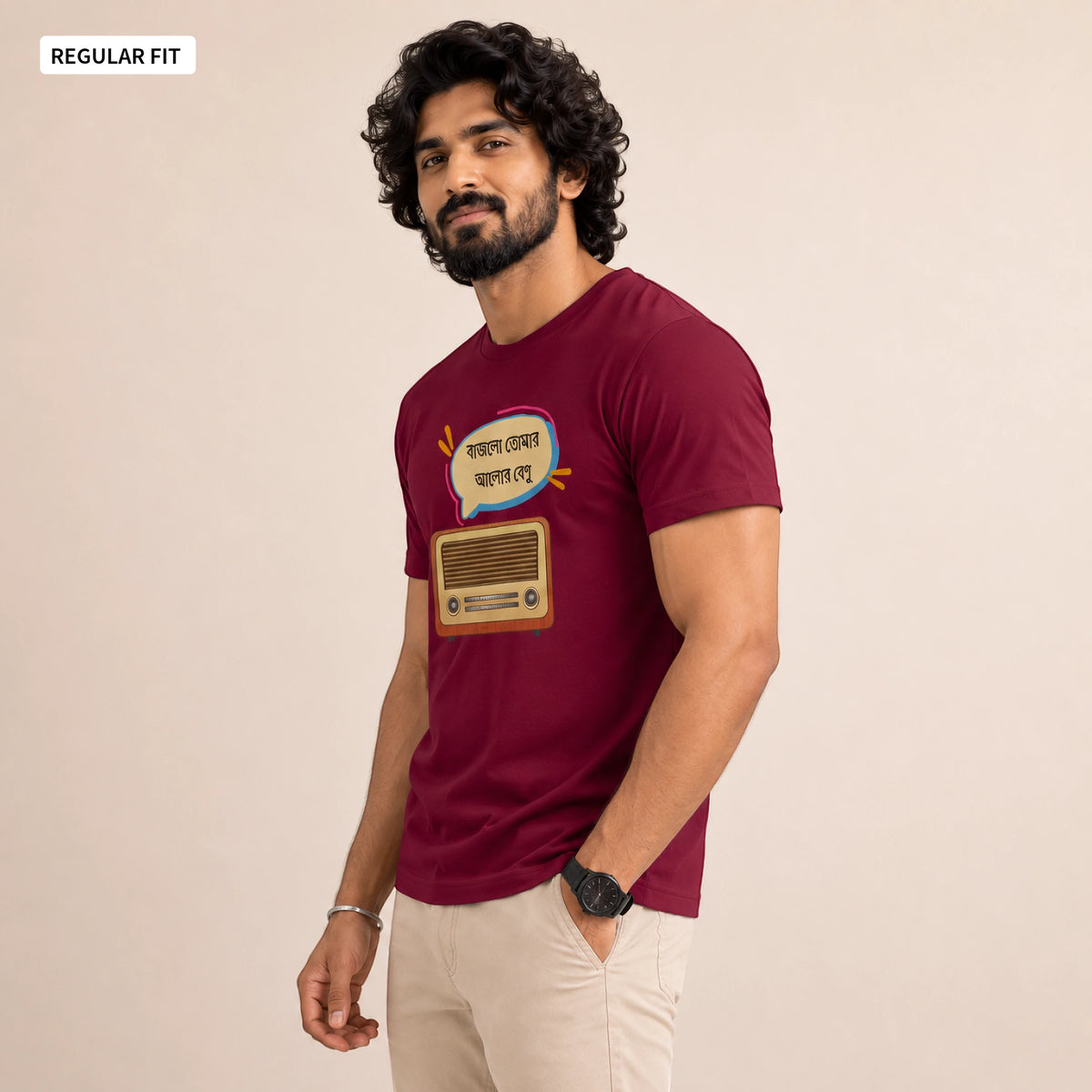 A man wearing a maroon short-sleeve t-shirt with a graphic print of a retro radio and Bengali text, paired with beige pants, standing against a plain beige background.