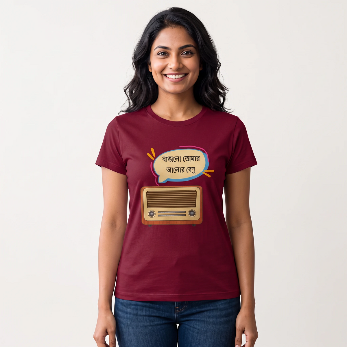A woman wearing a maroon short-sleeve graphic t-shirt with a cartoon radio and Bengali text bubble, paired with blue jeans, against a plain light background.