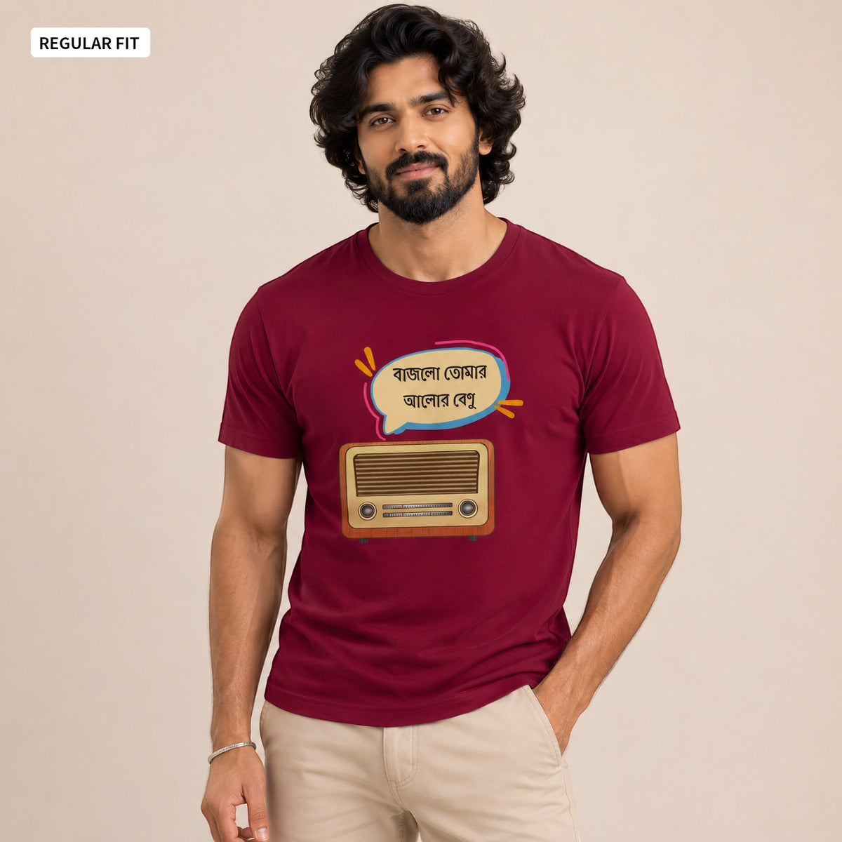 A man wearing a maroon short-sleeve t-shirt with a graphic of a retro radio and Bengali text inside a speech bubble, paired with beige pants, against a plain beige background.