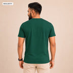 A man wearing a dark green short-sleeve t-shirt, viewed from the back, paired with beige trousers, against a solid beige background. A small label in the top-left corner reads 'REGULAR FIT'.