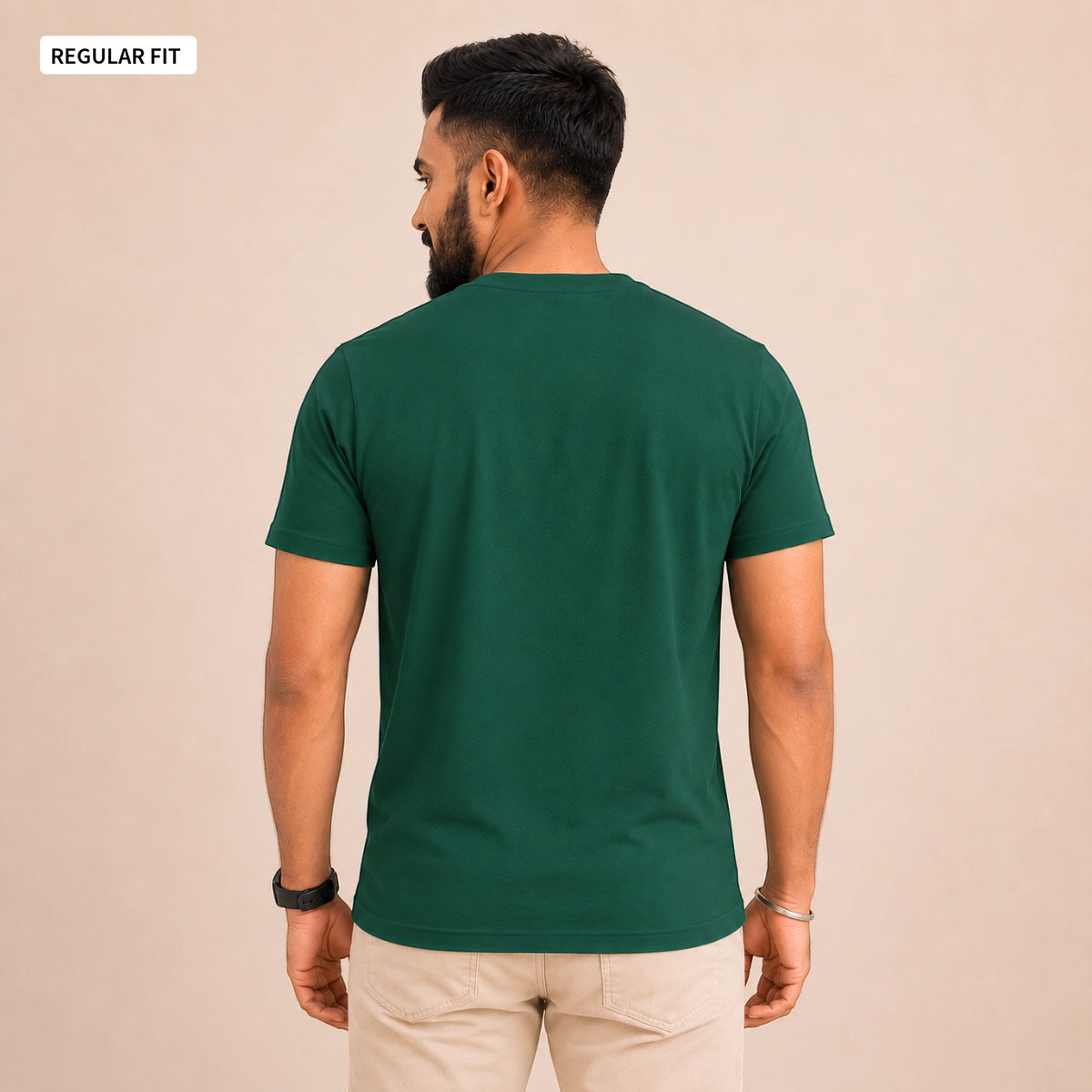 A man wearing a dark green short-sleeve t-shirt, viewed from the back, paired with beige trousers, against a solid beige background. A small label in the top-left corner reads 'REGULAR FIT'.