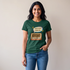 A woman wearing a dark green graphic t-shirt with a cartoon radio and Bengali text print, paired with blue jeans, standing against a plain beige wall.