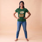 A woman modeling a dark green graphic t-shirt with a vintage radio and speech bubble design, paired with blue jeans, standing against a solid beige studio background.