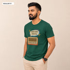 A man wearing a dark green short-sleeve t-shirt with a graphic of a vintage radio and Bengali text inside a speech bubble, paired with beige trousers, against a plain beige background.