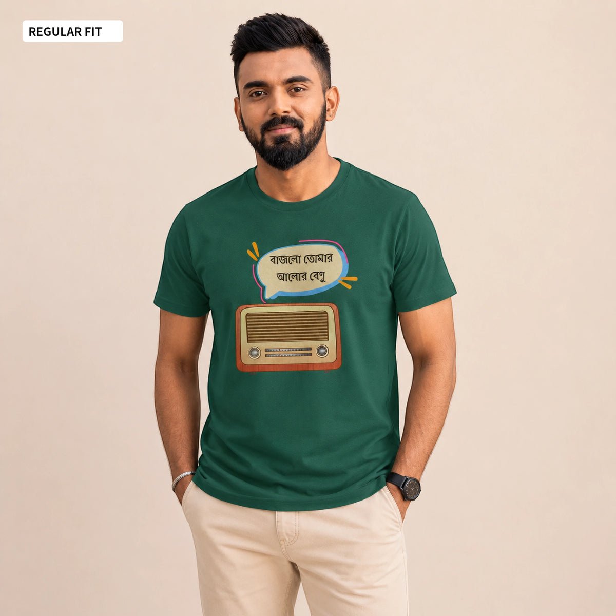 A man wearing a dark green graphic t-shirt with a retro radio and Bengali text design, paired with beige pants, standing against a solid beige background.
