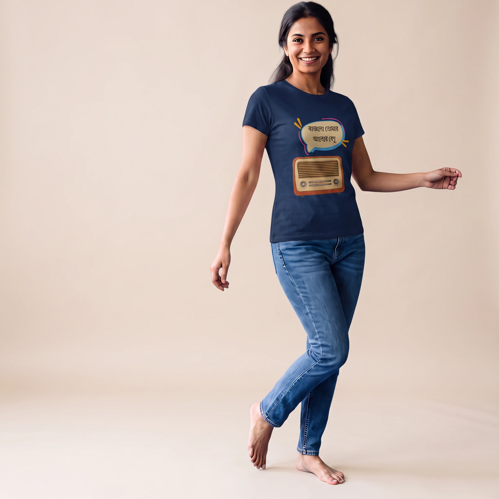 A woman modeling a navy blue graphic t-shirt with a retro radio design and the text 'Bajlo tomar alor benu'. She is wearing blue jeans and standing barefoot against a solid beige studio background.