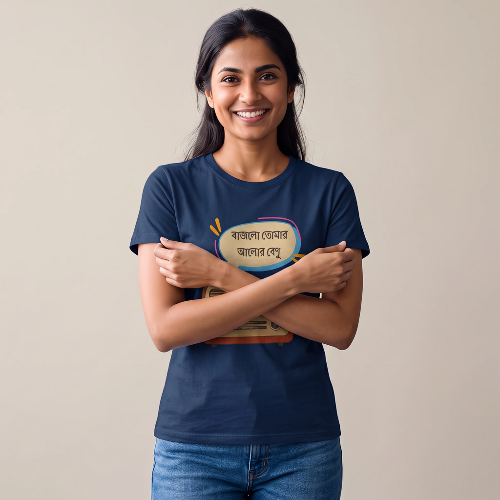 A smiling woman with dark hair stands against a plain beige background, wearing a navy blue t-shirt with a colorful graphic print in Bengali text and blue jeans.