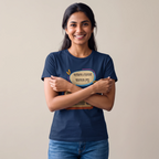 A smiling woman with dark hair stands against a plain beige background, wearing a navy blue t-shirt with a colorful graphic print in Bengali text and blue jeans.