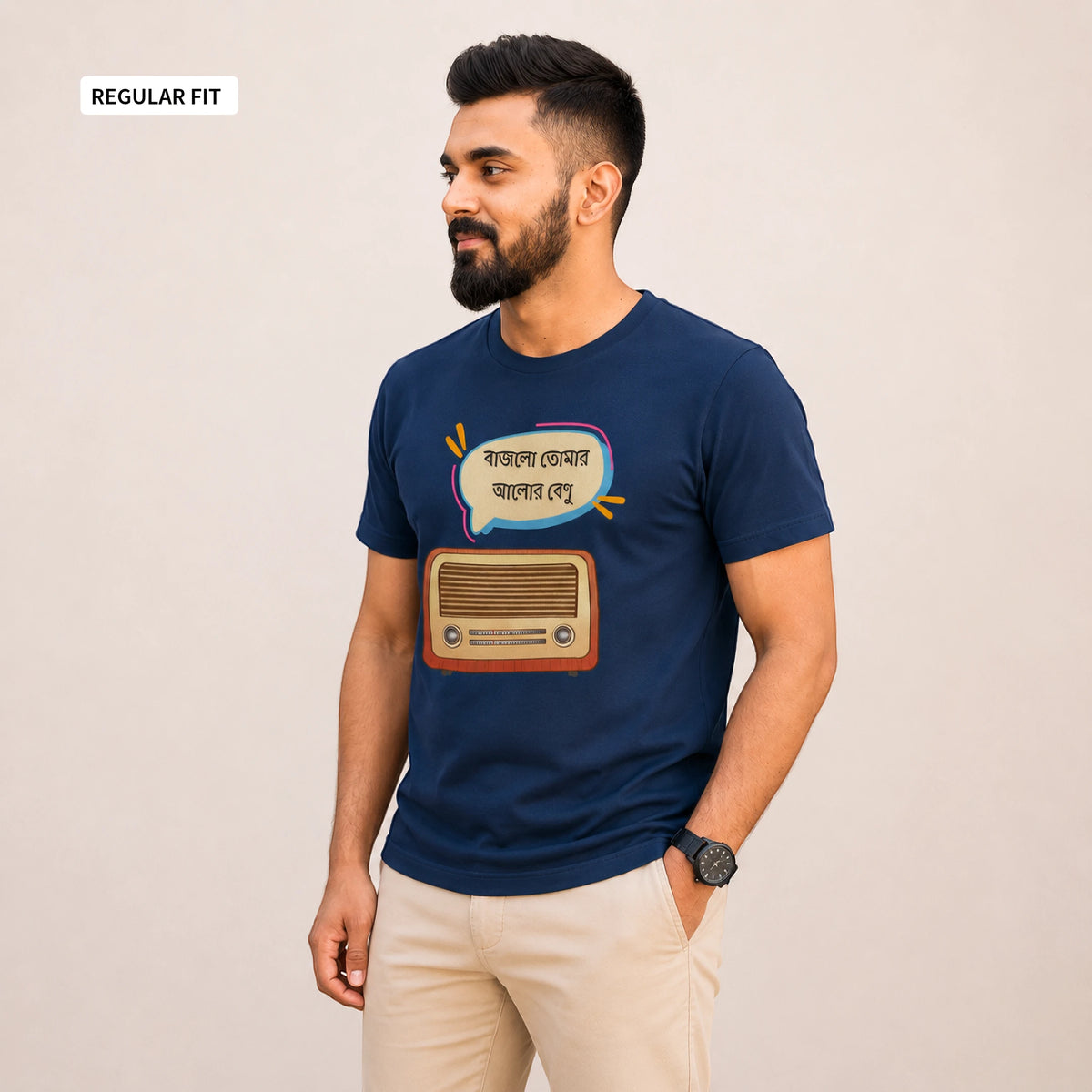 A man wearing a navy blue t-shirt with a graphic of a retro radio and a speech bubble in Bengali, paired with beige pants, standing against a plain beige background.