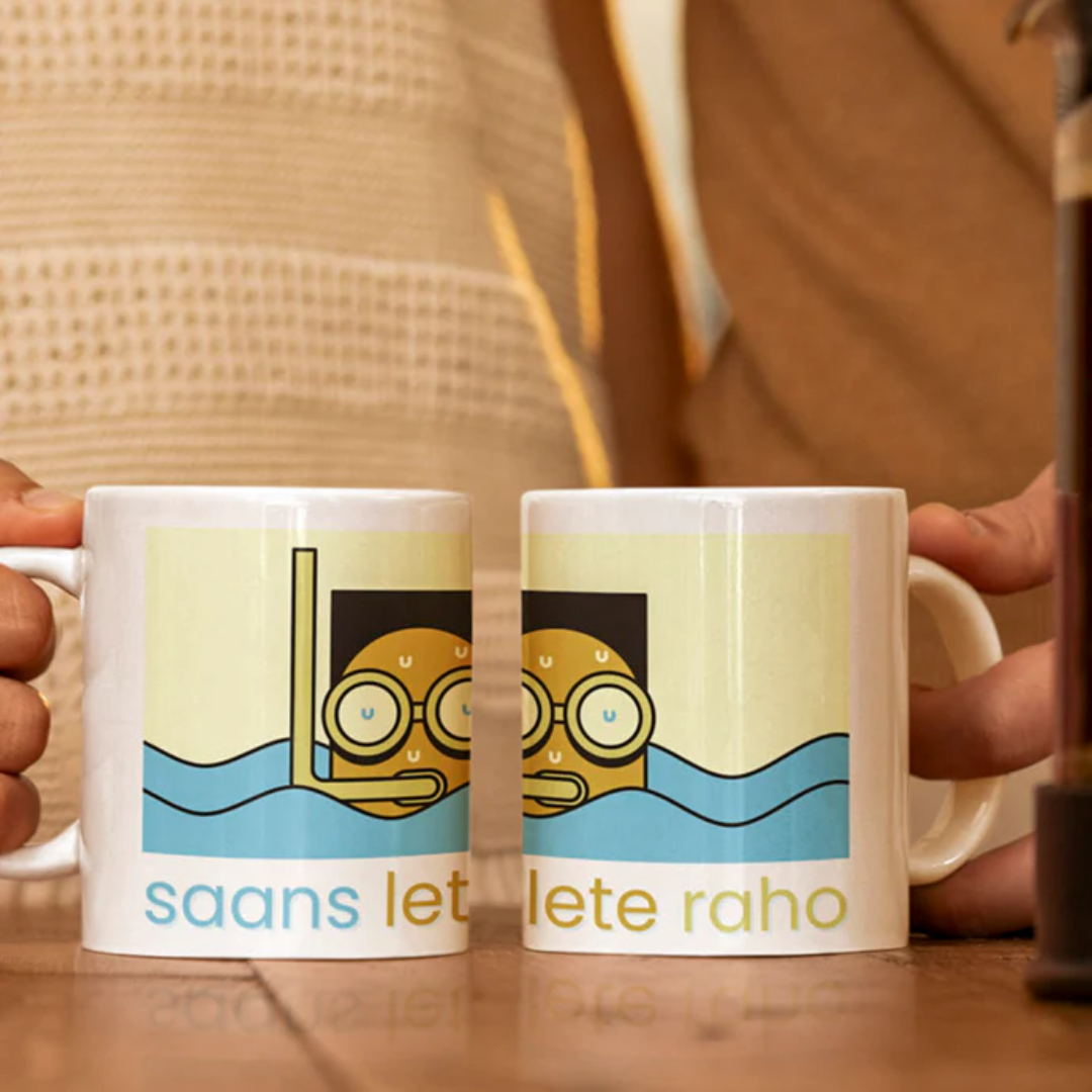 Two mugs with a cartoon character and text held by hands on a wooden surface.