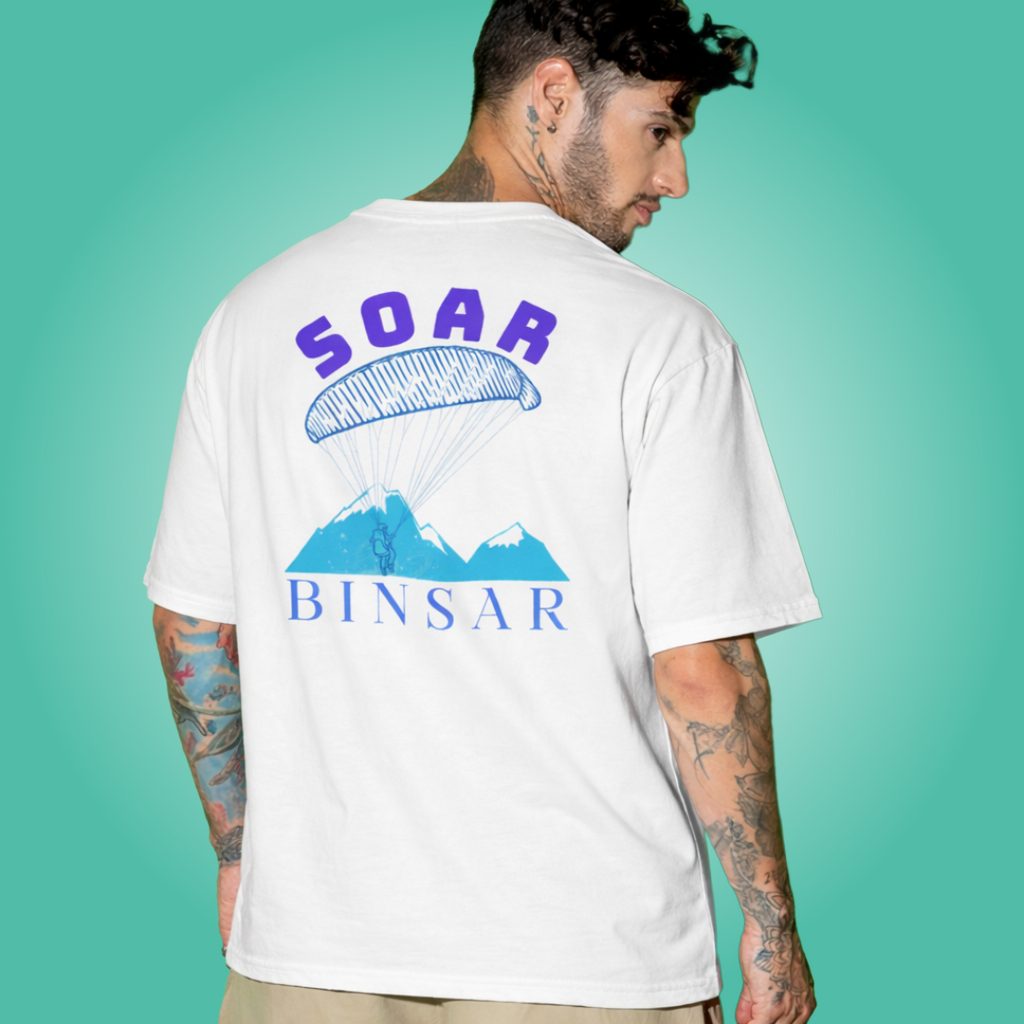 Person wearing a white t-shirt with 'SOAR BINSAR' design on the back against a teal background