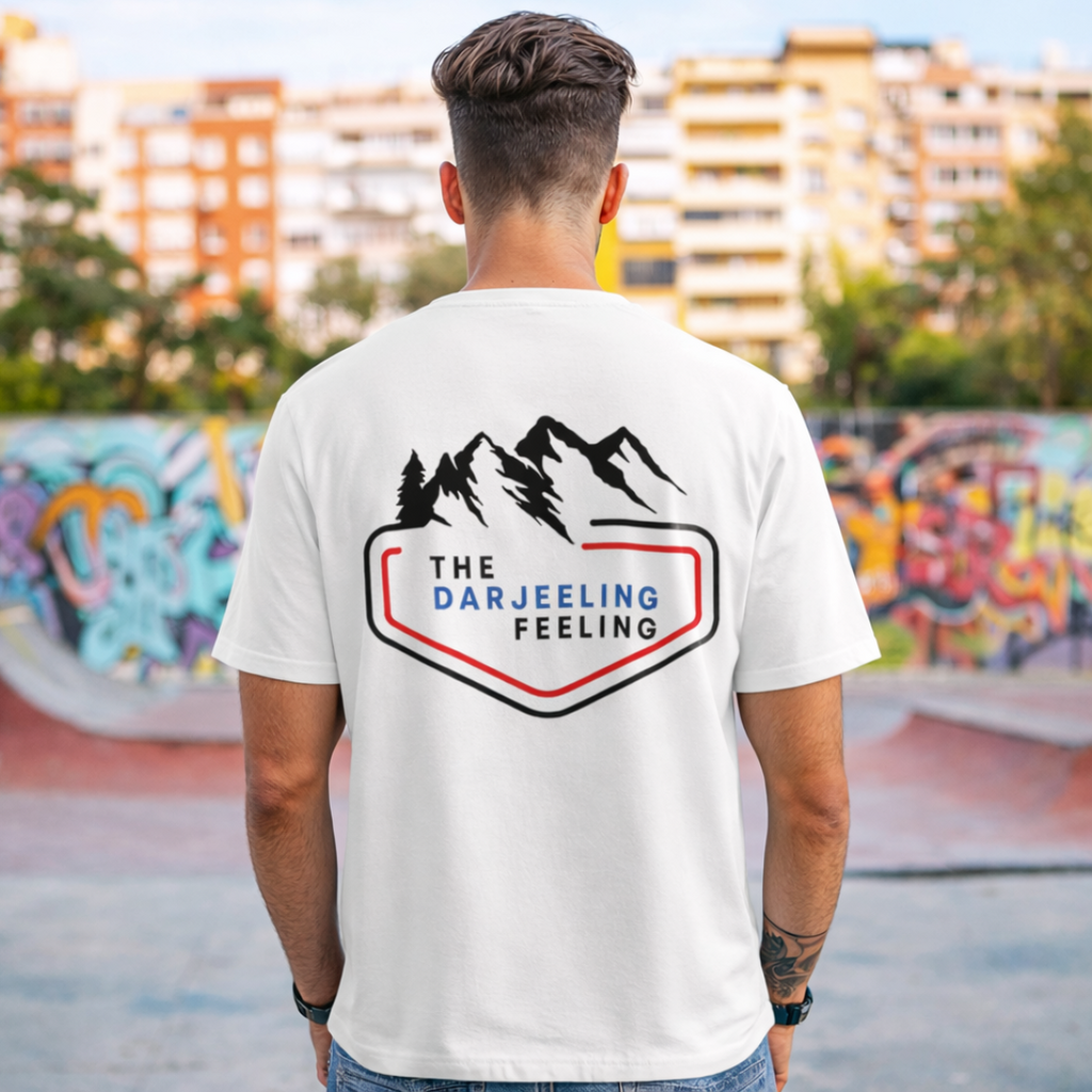 Person wearing a white t-shirt with 'The Darjeeling Feeling' logo in an urban setting.