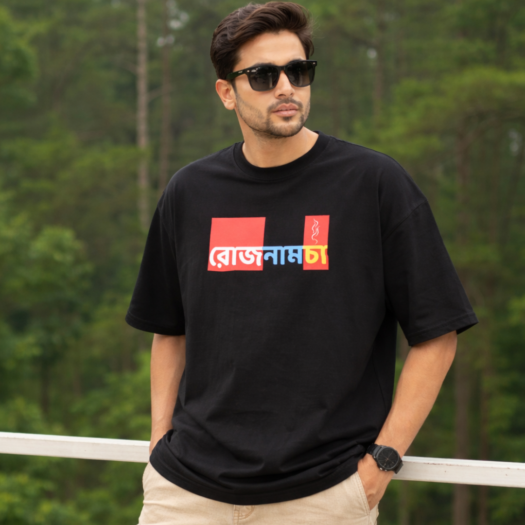 Man wearing a black t-shirt with colorful text, standing outdoors with greenery in the background