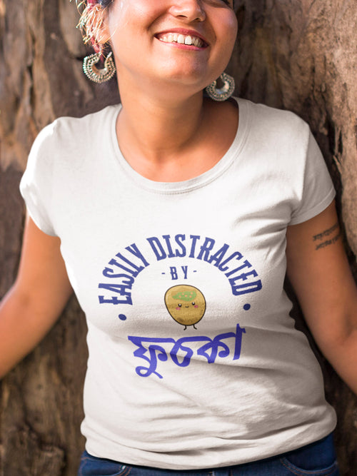 Person wearing a white t-shirt with blue text and graphics, standing against a natural background.
