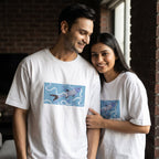 A man and a woman standing indoors wearing matching white T-shirts with a blue rectangular graphic of two fish on the front.