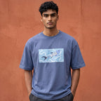 A man wearing a slate blue crewneck t-shirt with a graphic print of a koi fish on a light blue background, standing against a textured terracotta wall.
