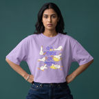 A woman modeling a light purple t-shirt with a cartoon graphic of geese and a teapot in Bengali script, paired with dark blue jeans against a dark green background.