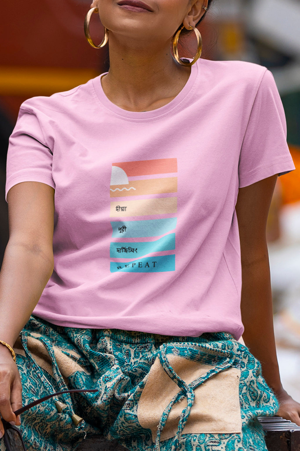 Person wearing a pink t-shirt with a graphic design, sitting outdoors.
