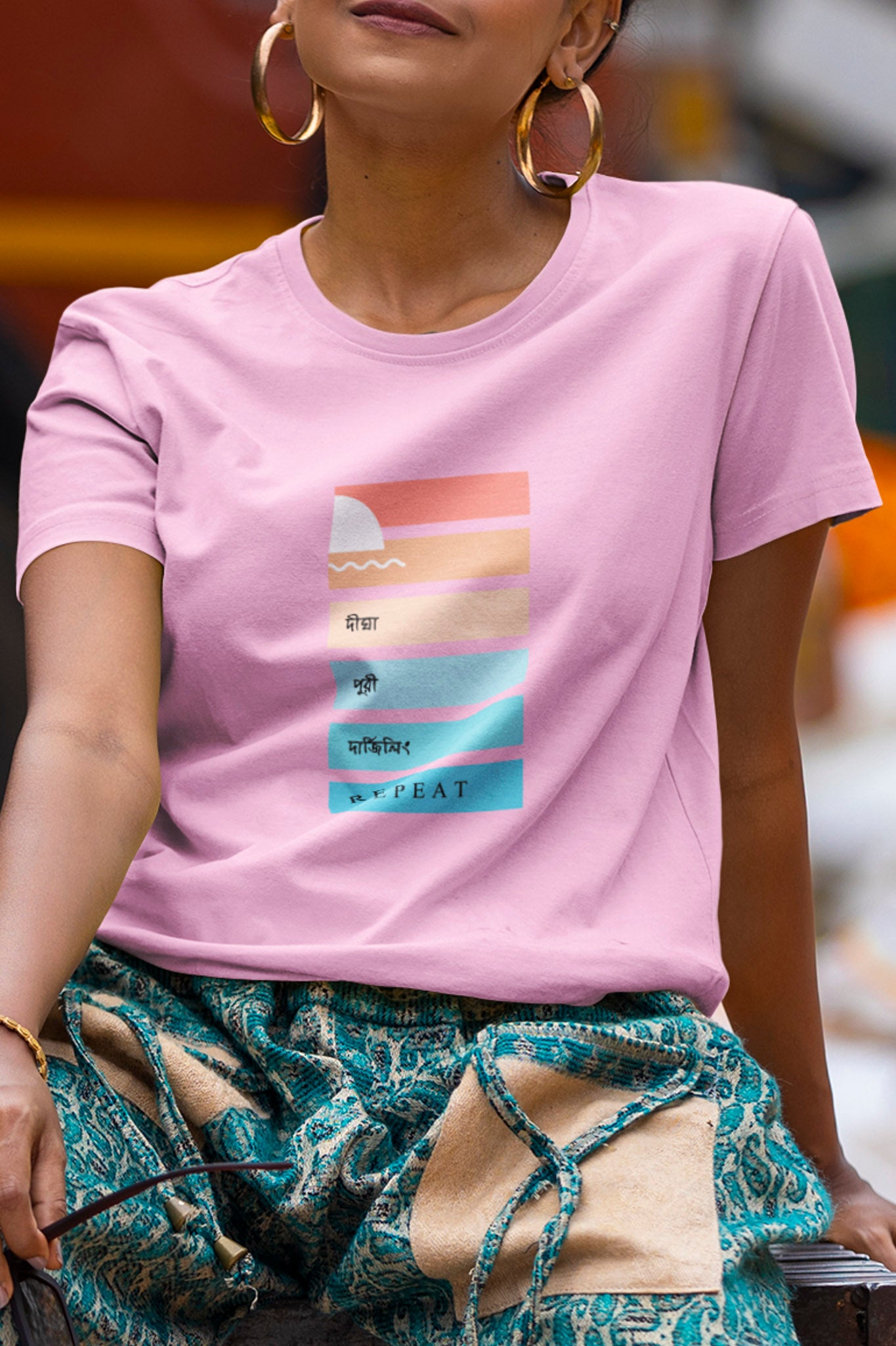 Person wearing a pink t-shirt with a graphic design, sitting outdoors.